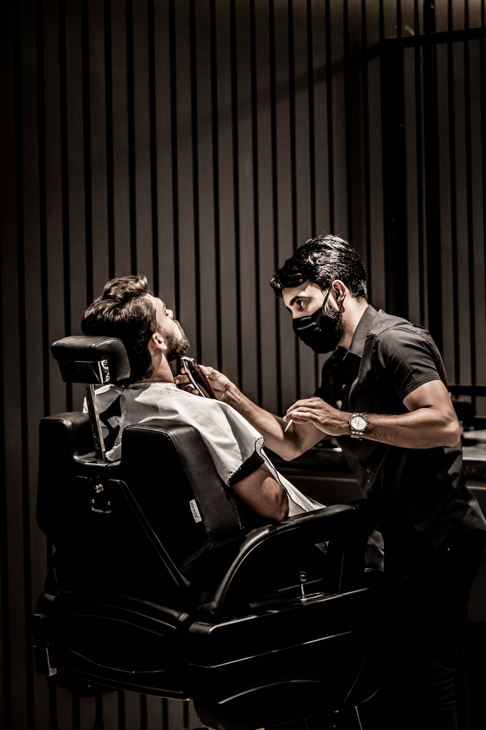 A client reclined in a black leather chair against a wall of dark slatted wood