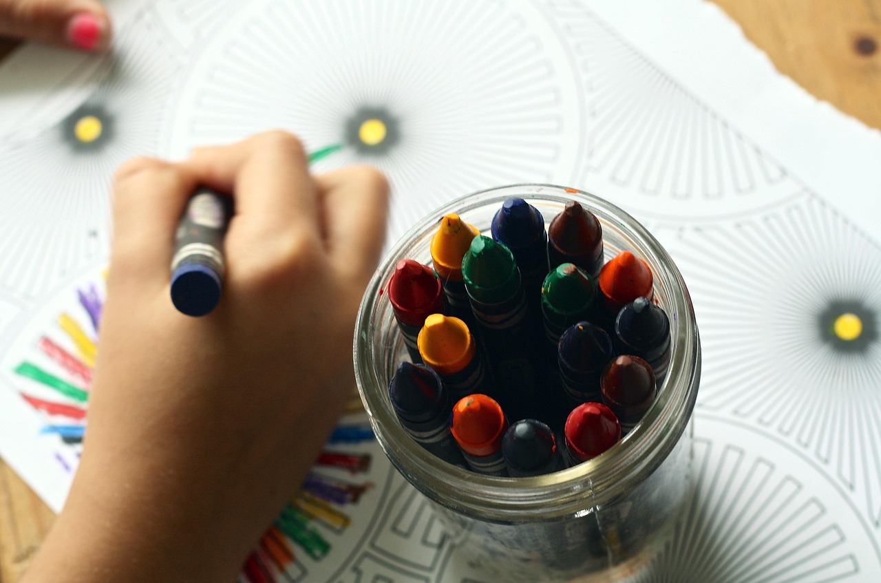 A child's hand colouring with a jar of crayons