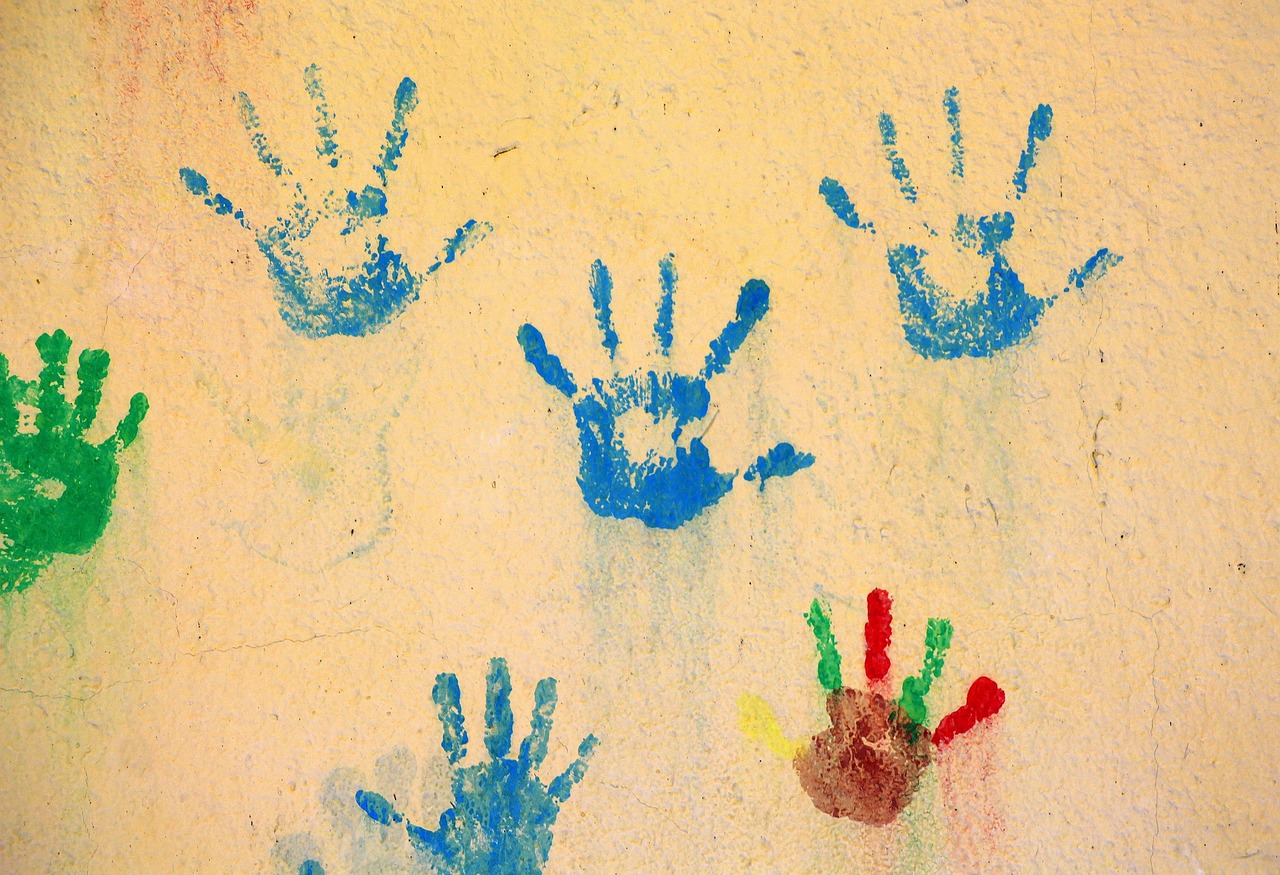 Painted children's handprints in blue and green on a sunny yellow wall
