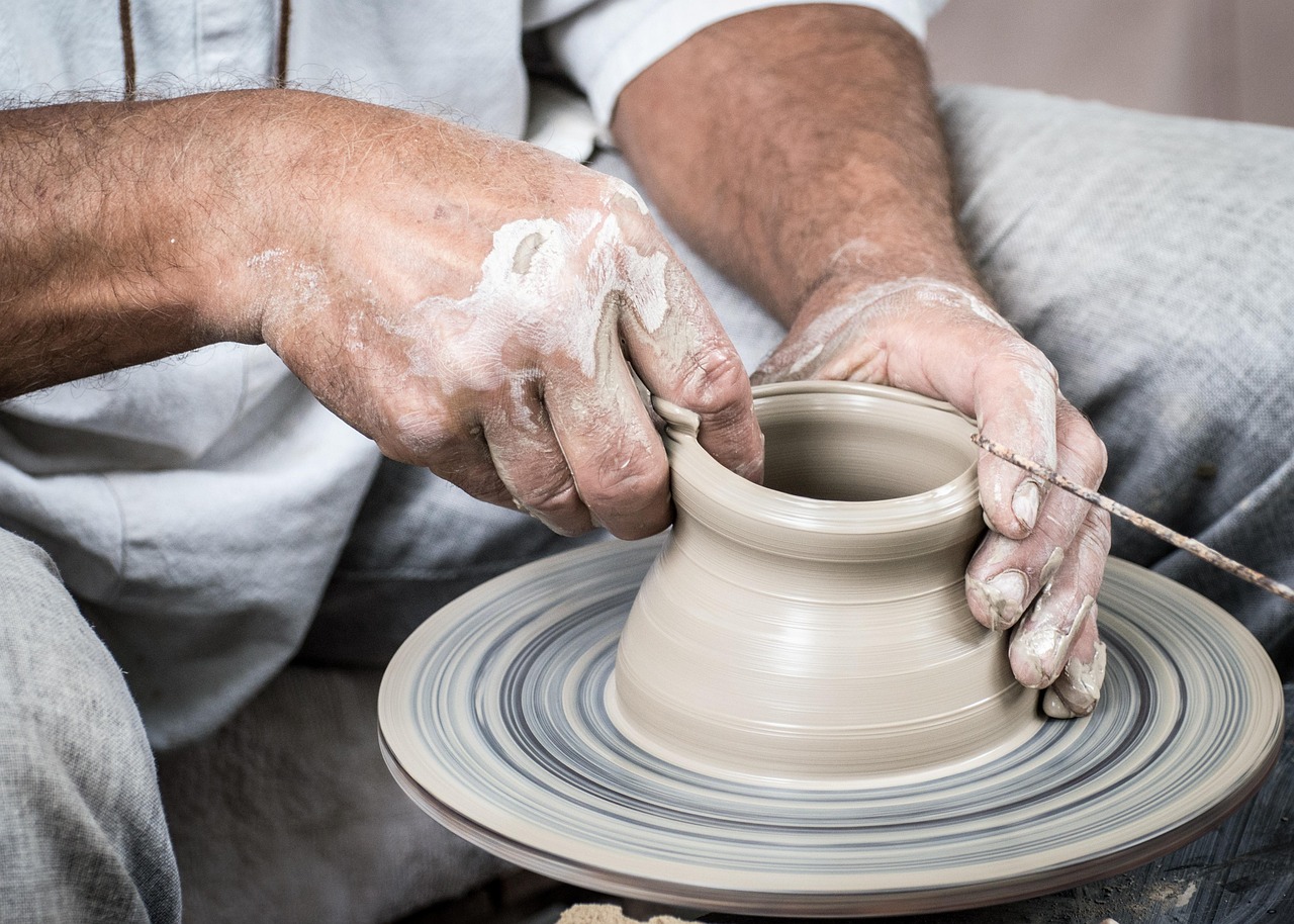 Clay-covered hands shaping a vessel on the wheel