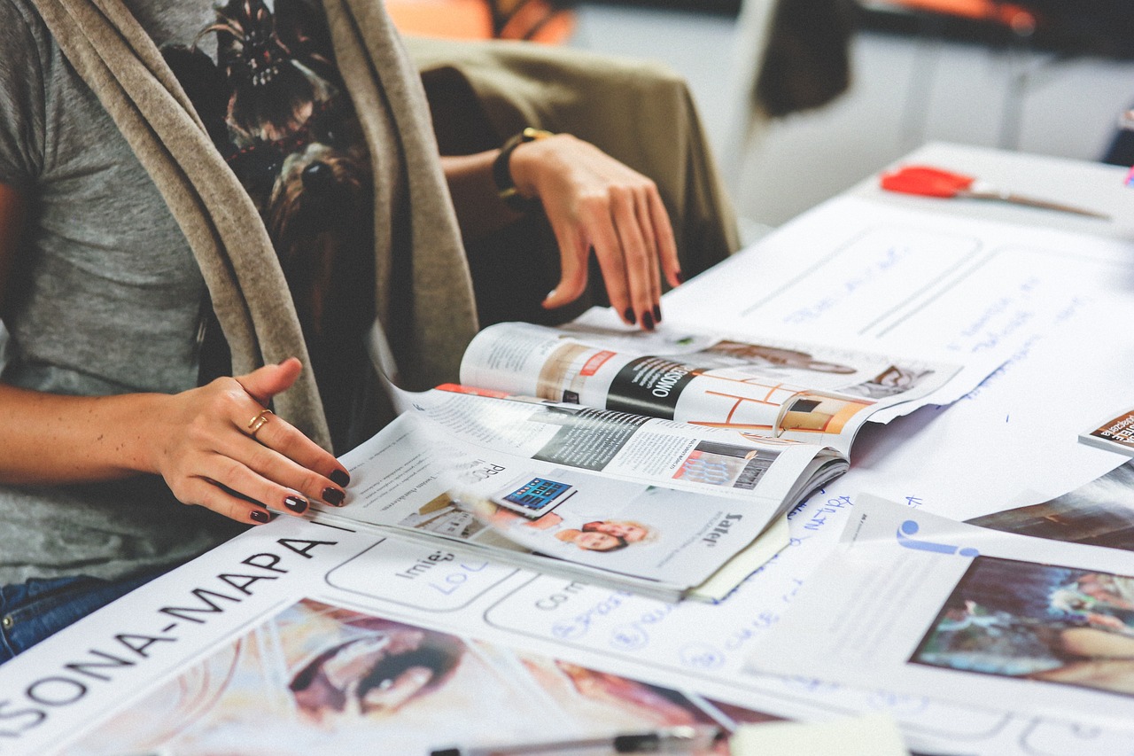 Hands working across magazine layout proofs on a desk