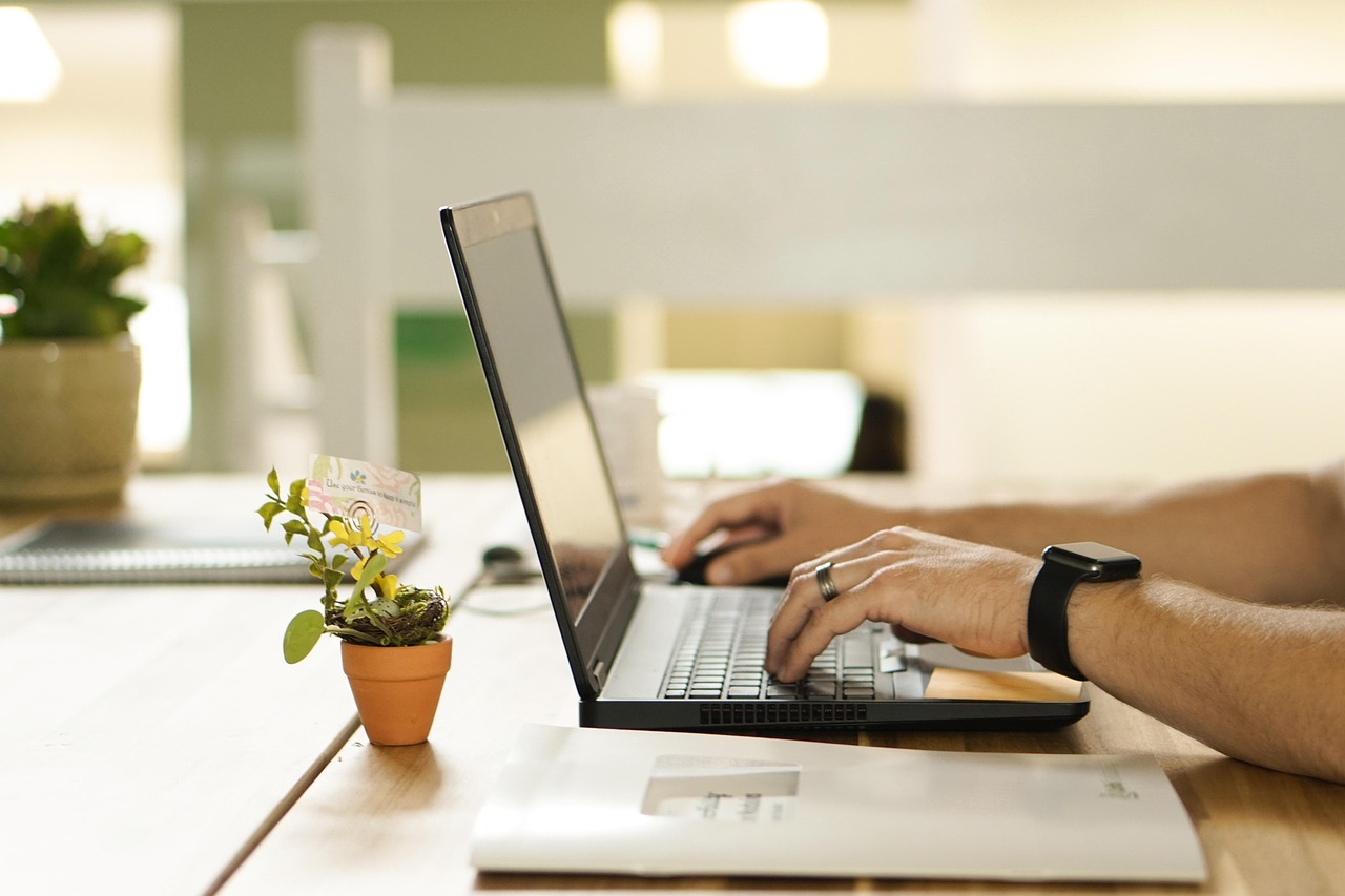 Hands typing on a laptop at a warm wooden desk