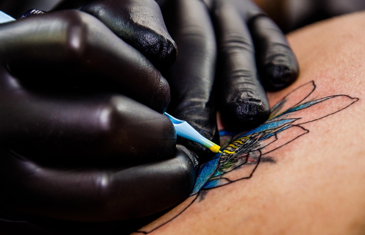 Black-gloved hands guiding a tattoo machine through a colour piece
