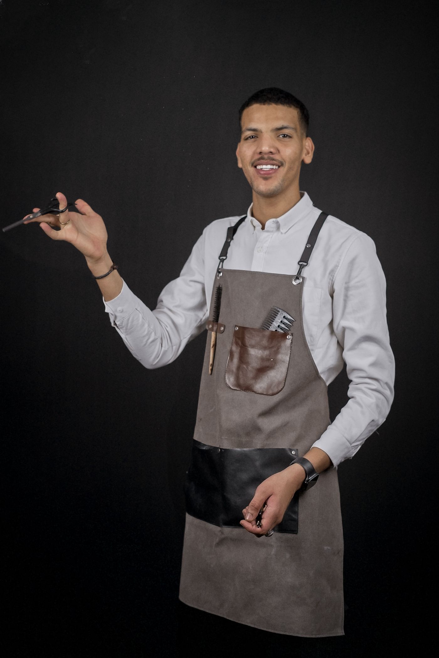 A barber in a leather apron standing against a dark wall
