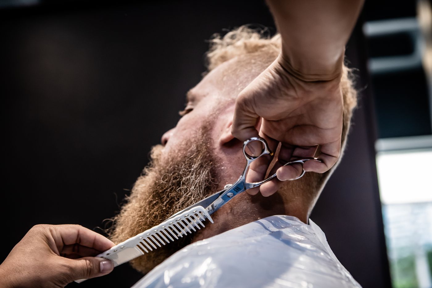 Scissors trimming a full beard against a dark background