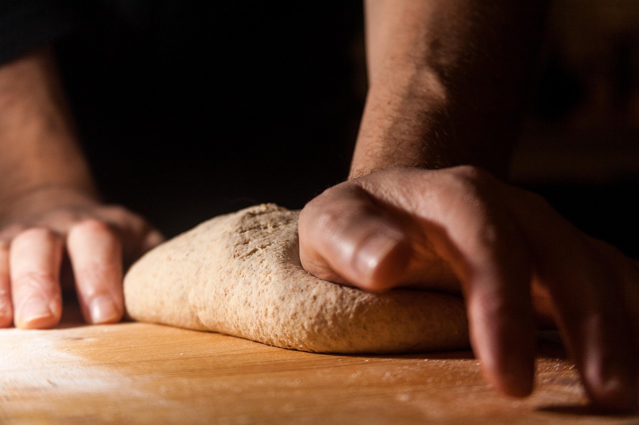 A baker's hands folding dough on a wooden bench in low light