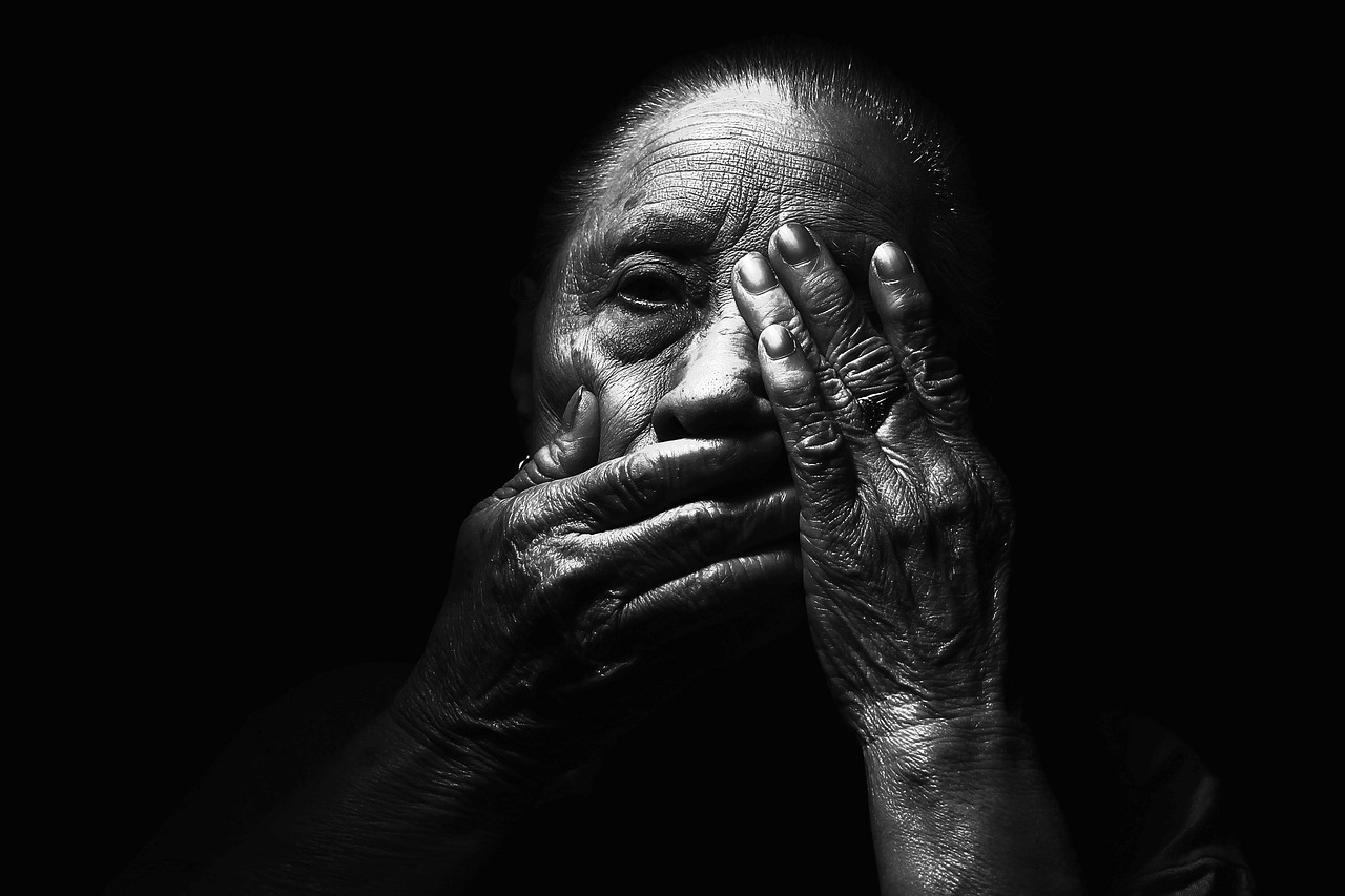 An elderly woman's hands held over her face, in monochrome