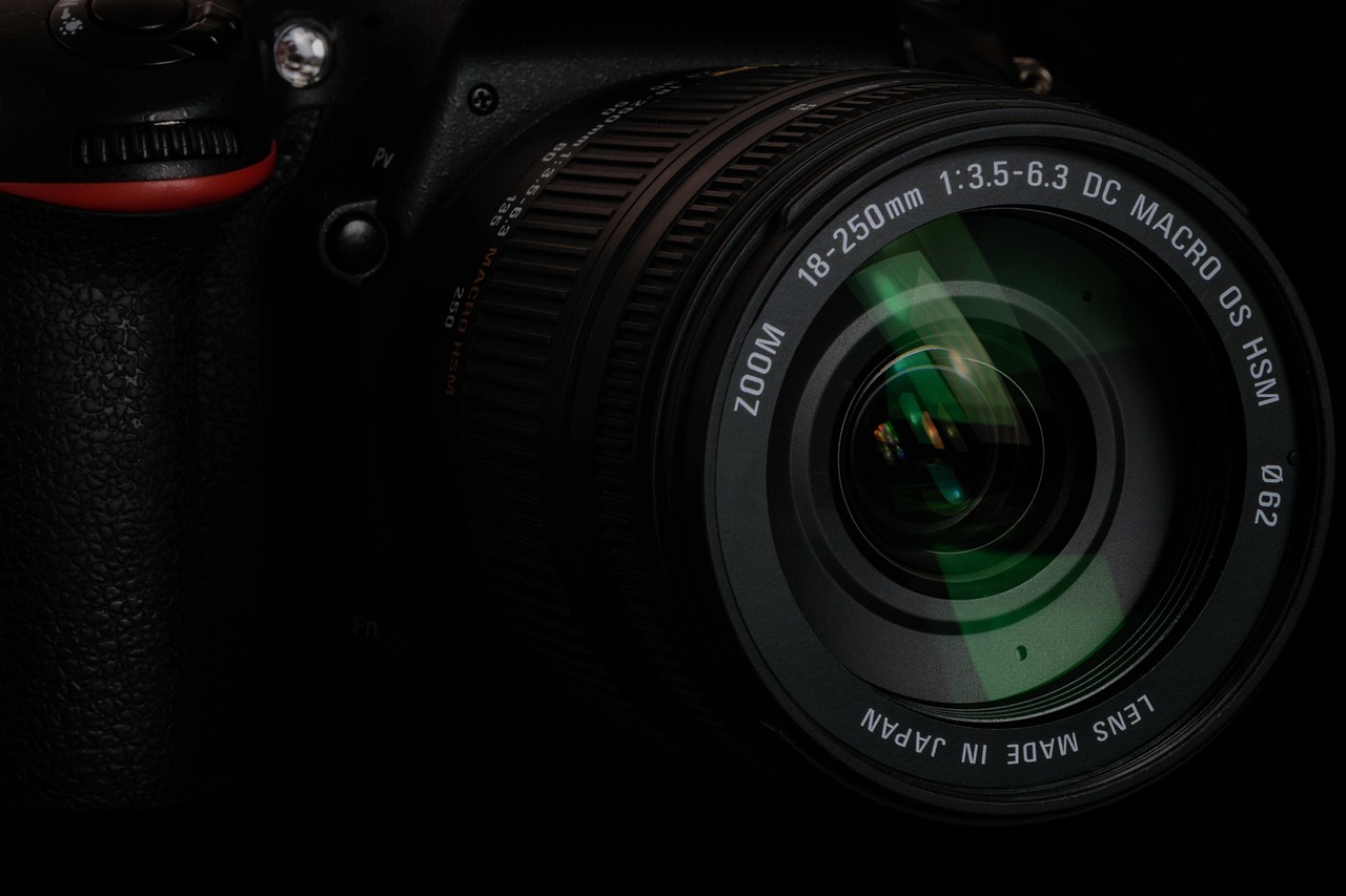 A camera lens in near-darkness, the glass catching a sliver of light