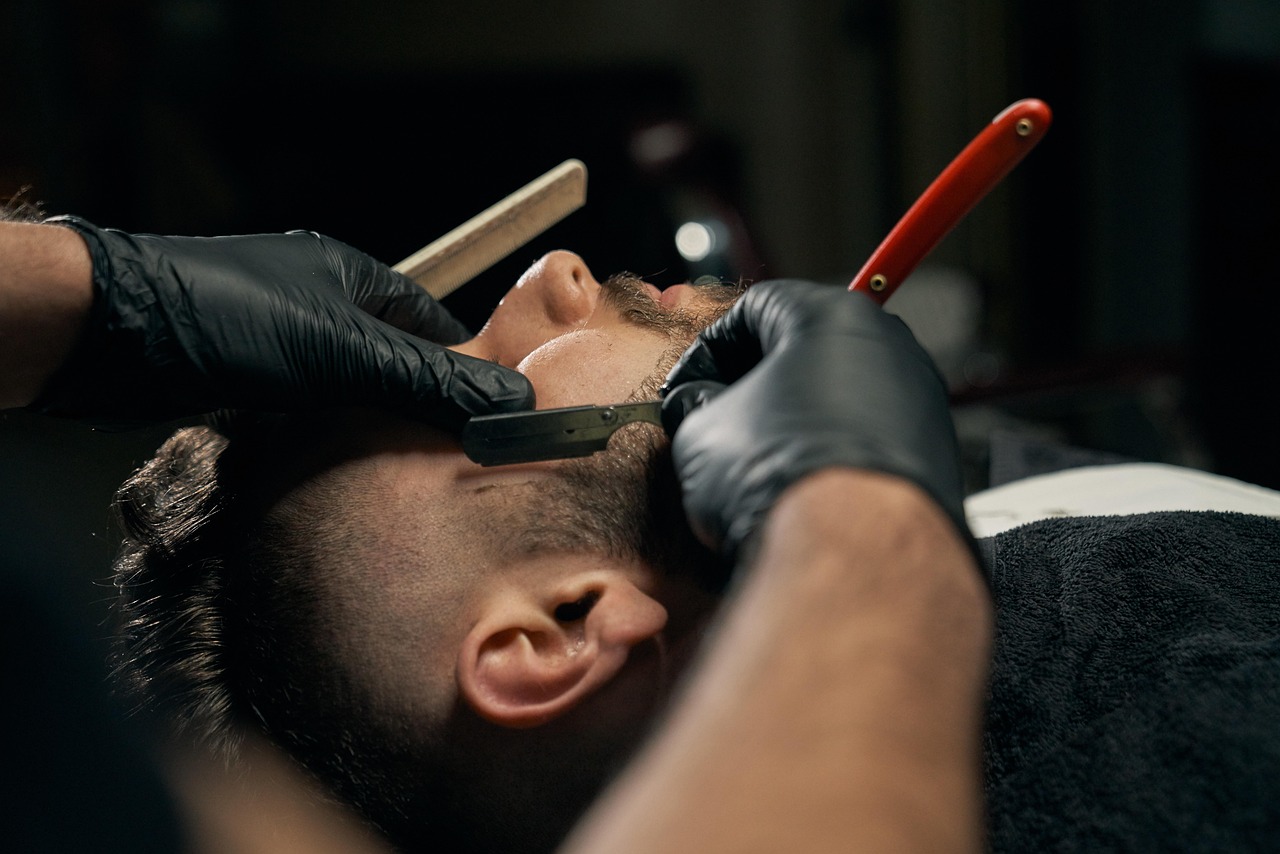 A straight-razor shave under low light, the blade catching the lamp