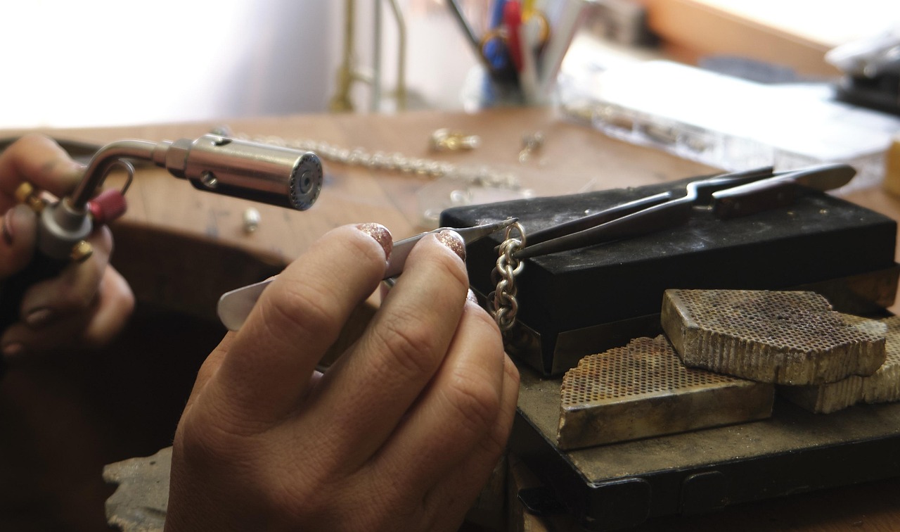 A goldsmith's hands soldering a silver chain at the bench