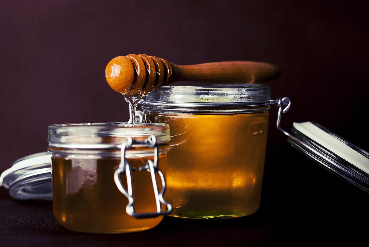 Two glass jars of honey with a wooden dipper