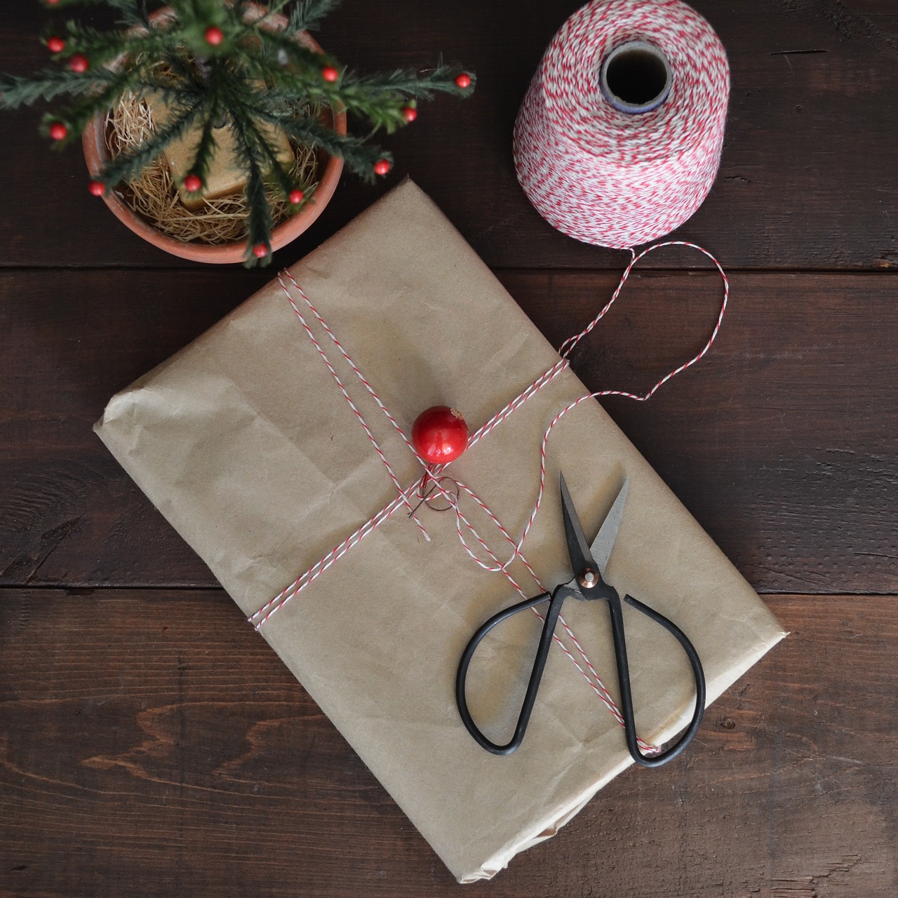 A parcel wrapped in kraft paper and twine with black scissors on dark wood