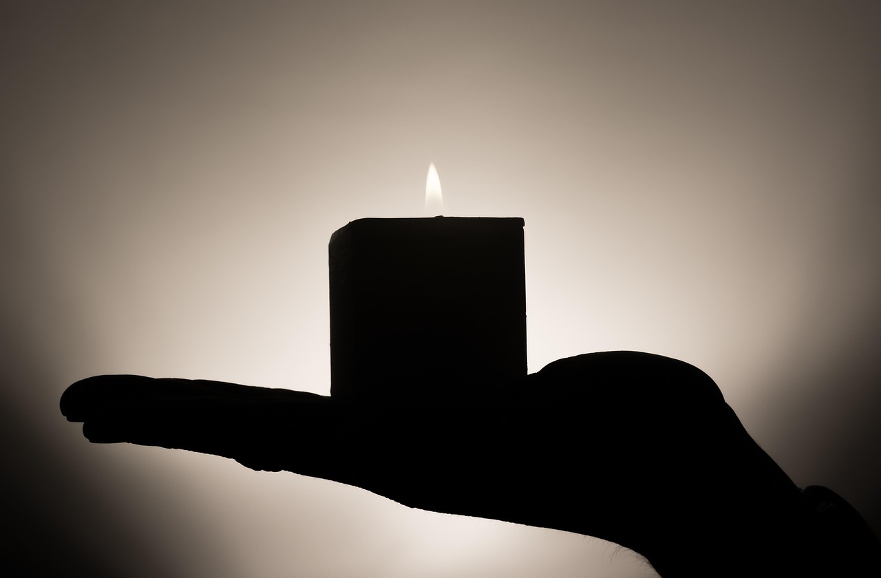 A candle held on an open palm in warm half-dark