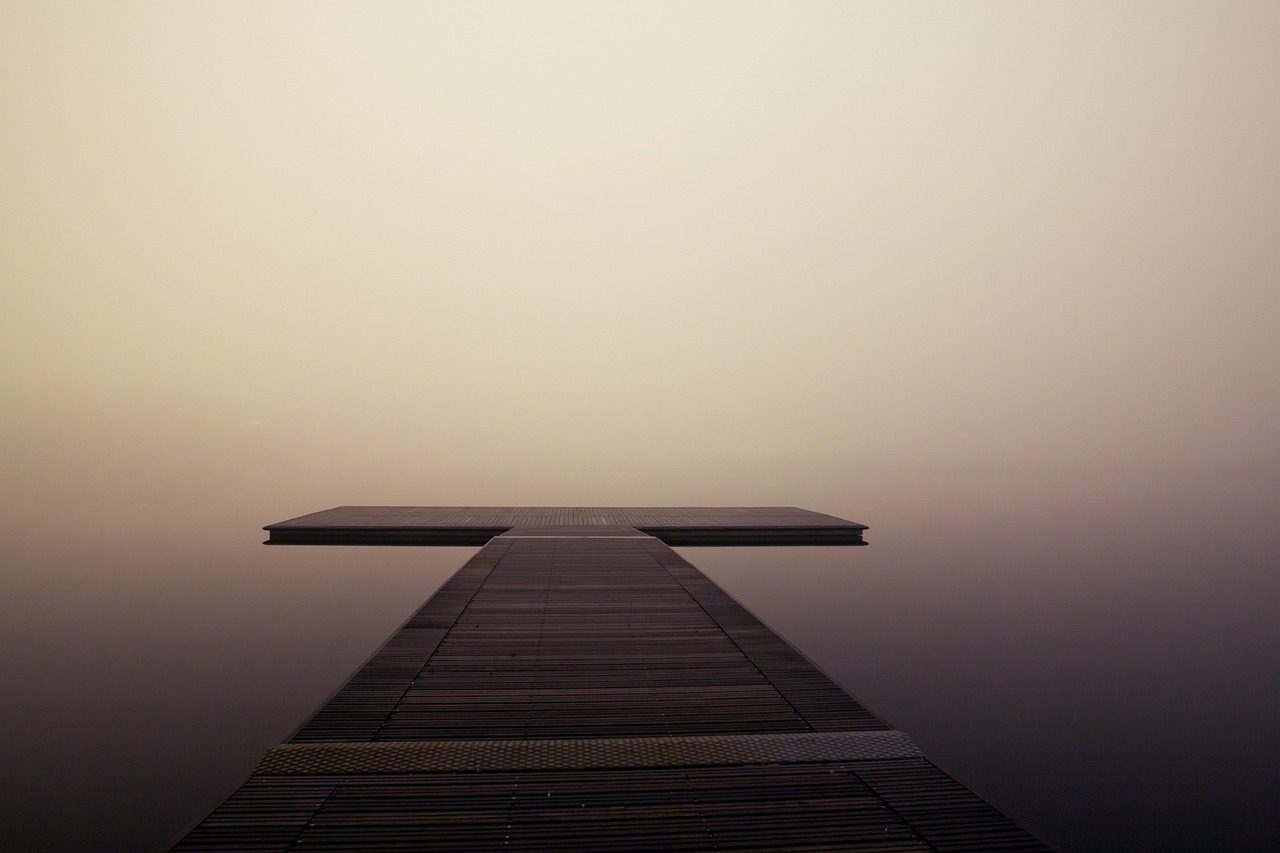 A wooden jetty reaching into still, misted water