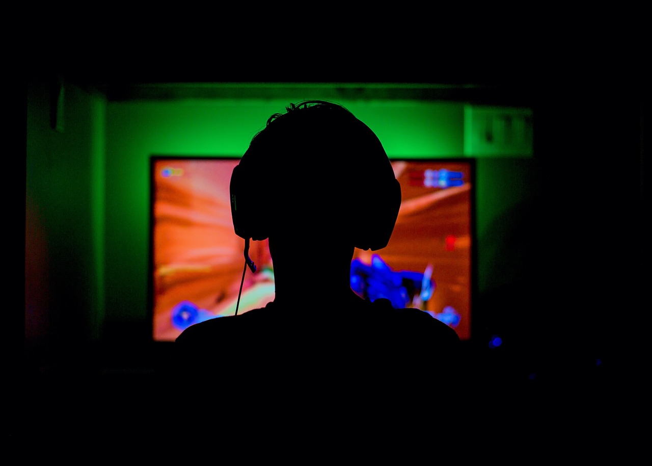 A player silhouetted against a glowing screen in headphones