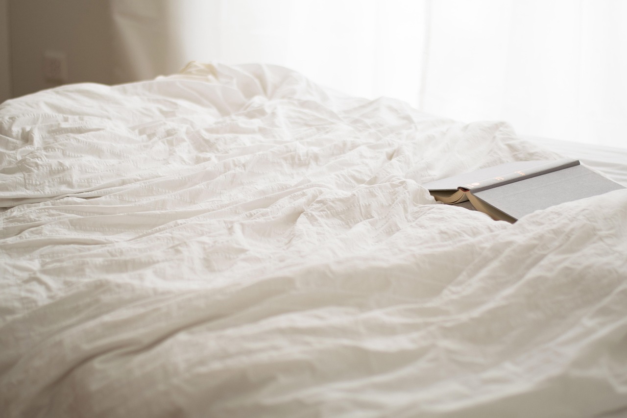 Rumpled white linen and an open book in soft morning light